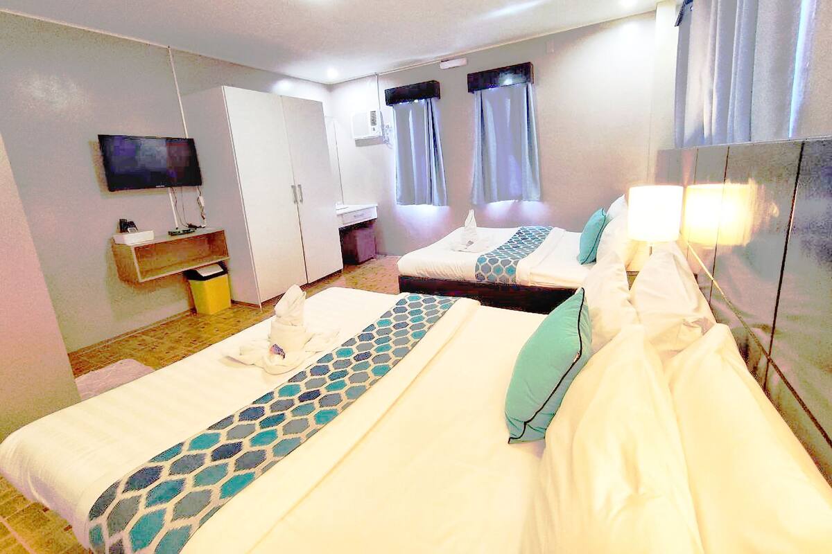 A hotel room with two beds, a TV, a mirror, and a bathroom.