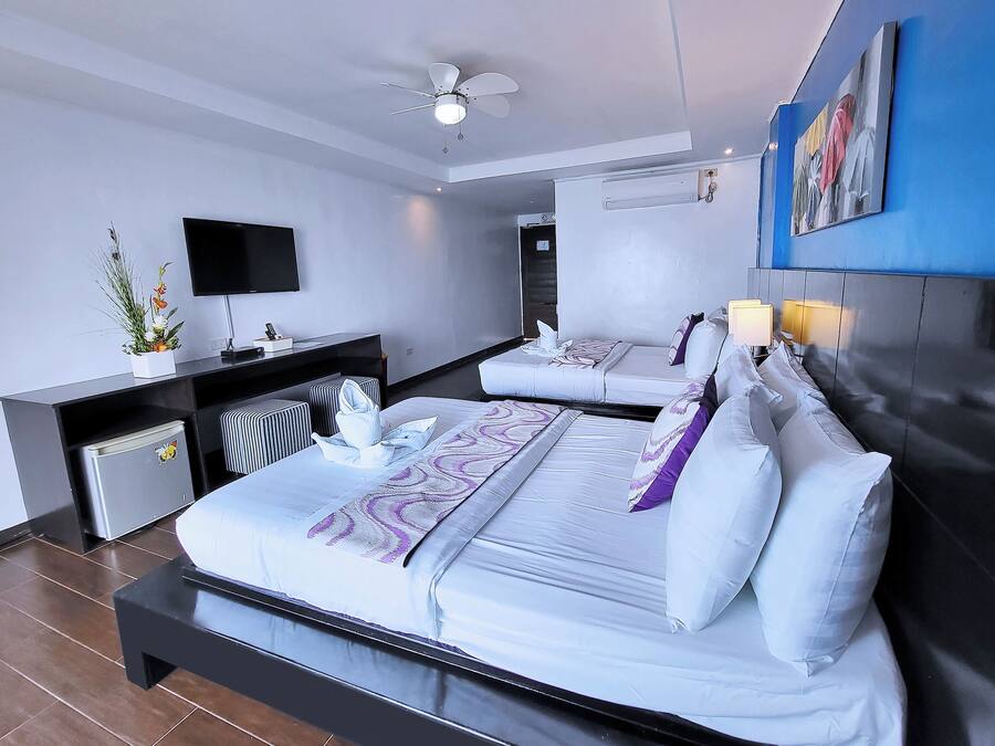 Une chambre d’hôtel moderne équipée de deux lits, d’un téléviseur à écran plat, d’un bureau avec un ordinateur et d’un ventilateur de plafond.