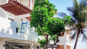 A hotel entrance with a 'WELCOME' sign, a covered parking area, and a view of the sea.