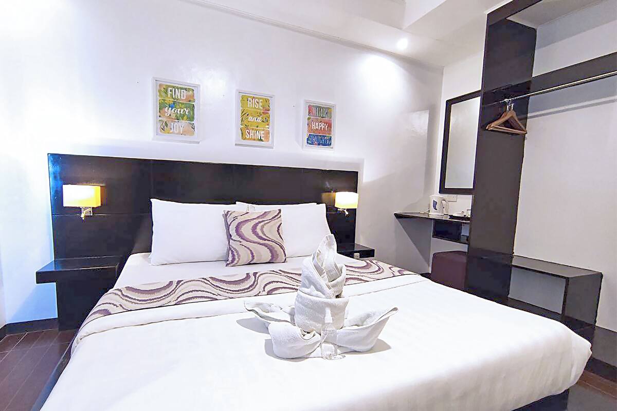 A hotel room with a large bed, two bedside lamps, a nightstand, a mirror, and three motivational posters on the wall.