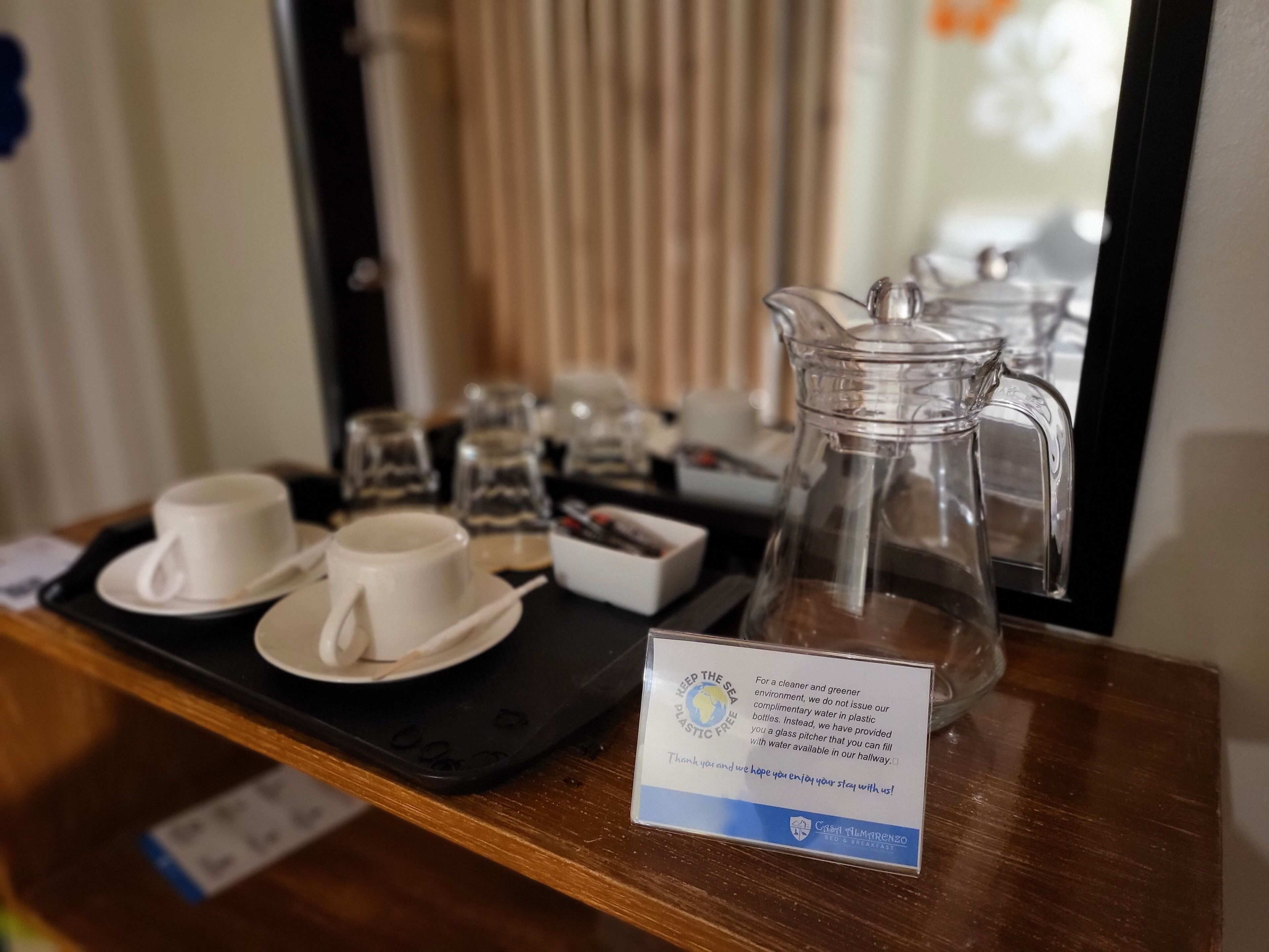 Una bandeja con una jarrón de vidrio, dos tazas y un cartel que promociona botellas de agua sin plástico.