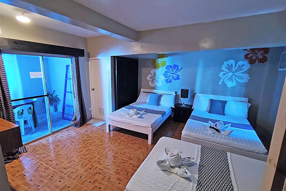 A hotel room with two beds, a small table, and a view of the outside.
