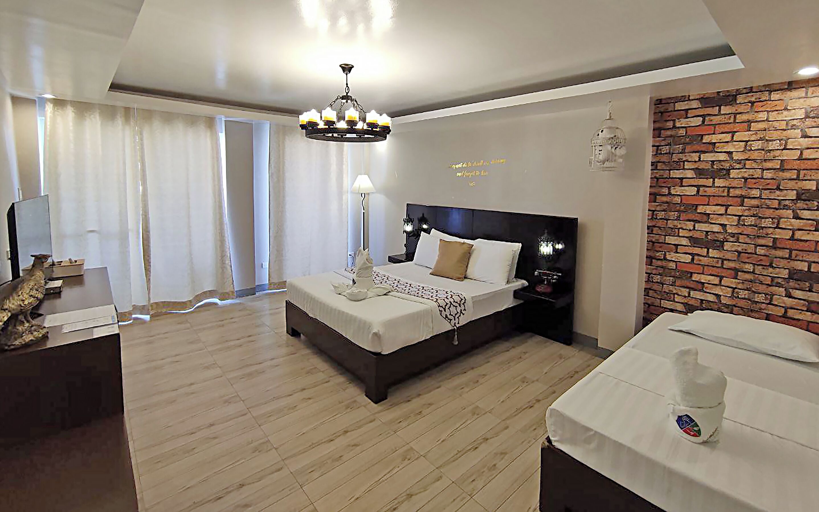A modern hotel room with a large bed, a desk, and a brick accent wall.
