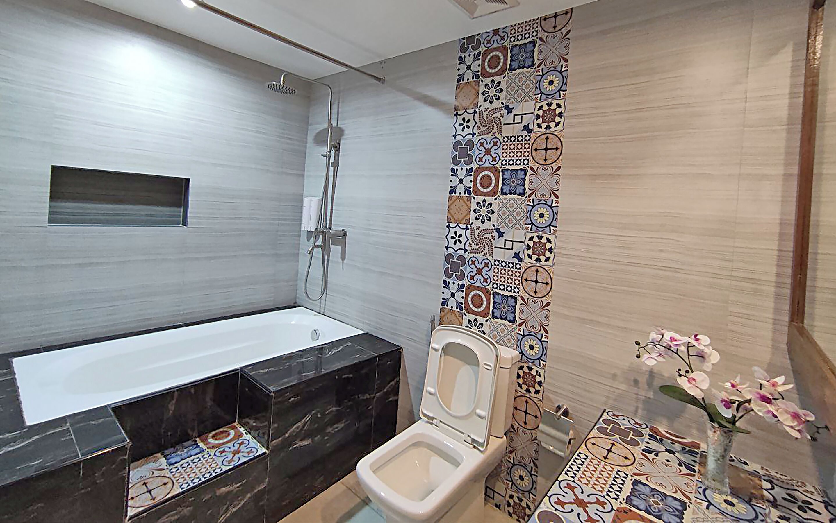 A modern bathroom with a bathtub, shower, and toilet. The walls are decorated with patterned tiles.