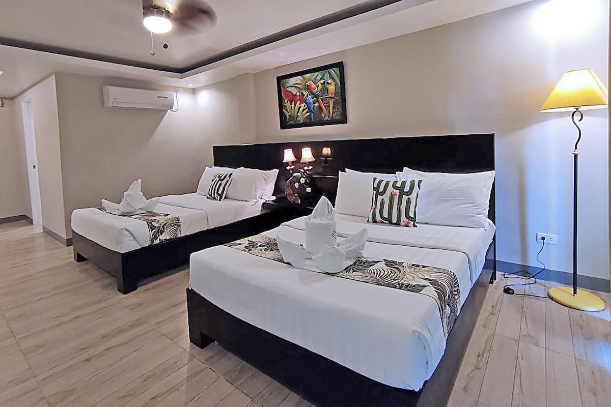 A hotel room with two beds, a ceiling fan, an air conditioning unit, a painting, and a lamp.