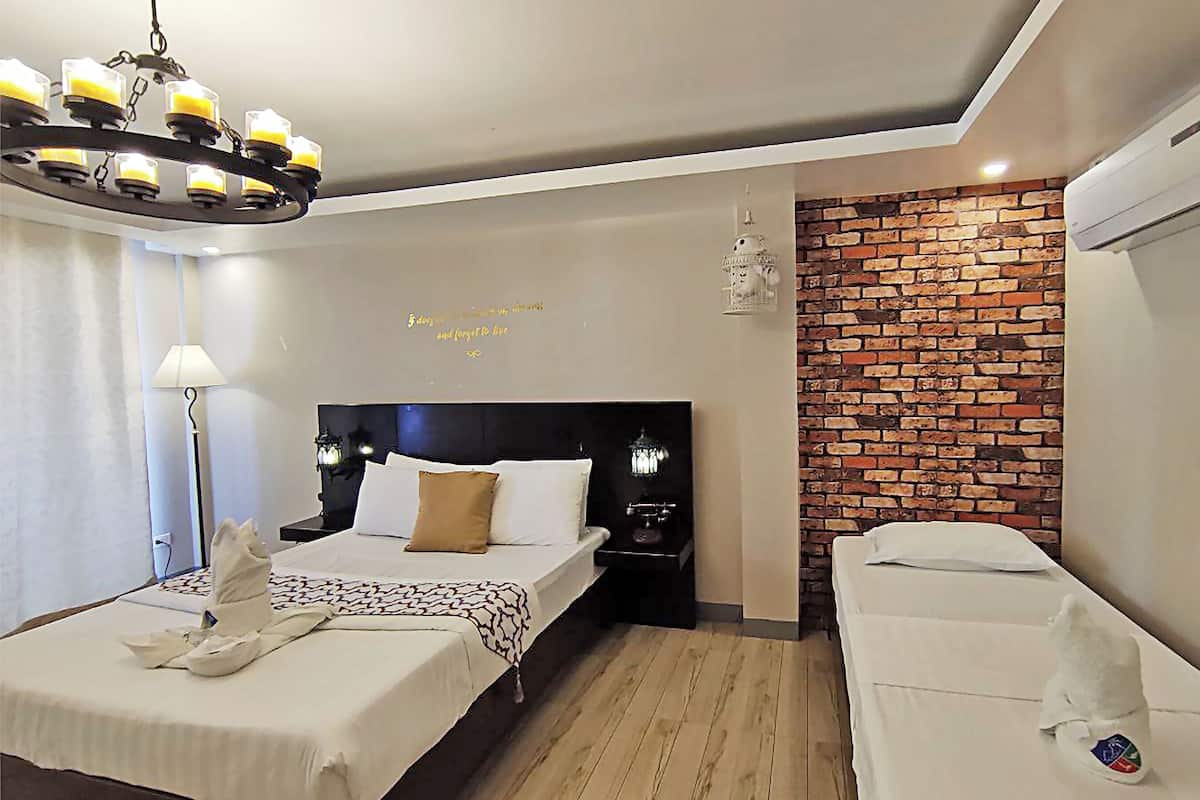 A hotel room with a bed, bedside table, lamp, and a brick wall.