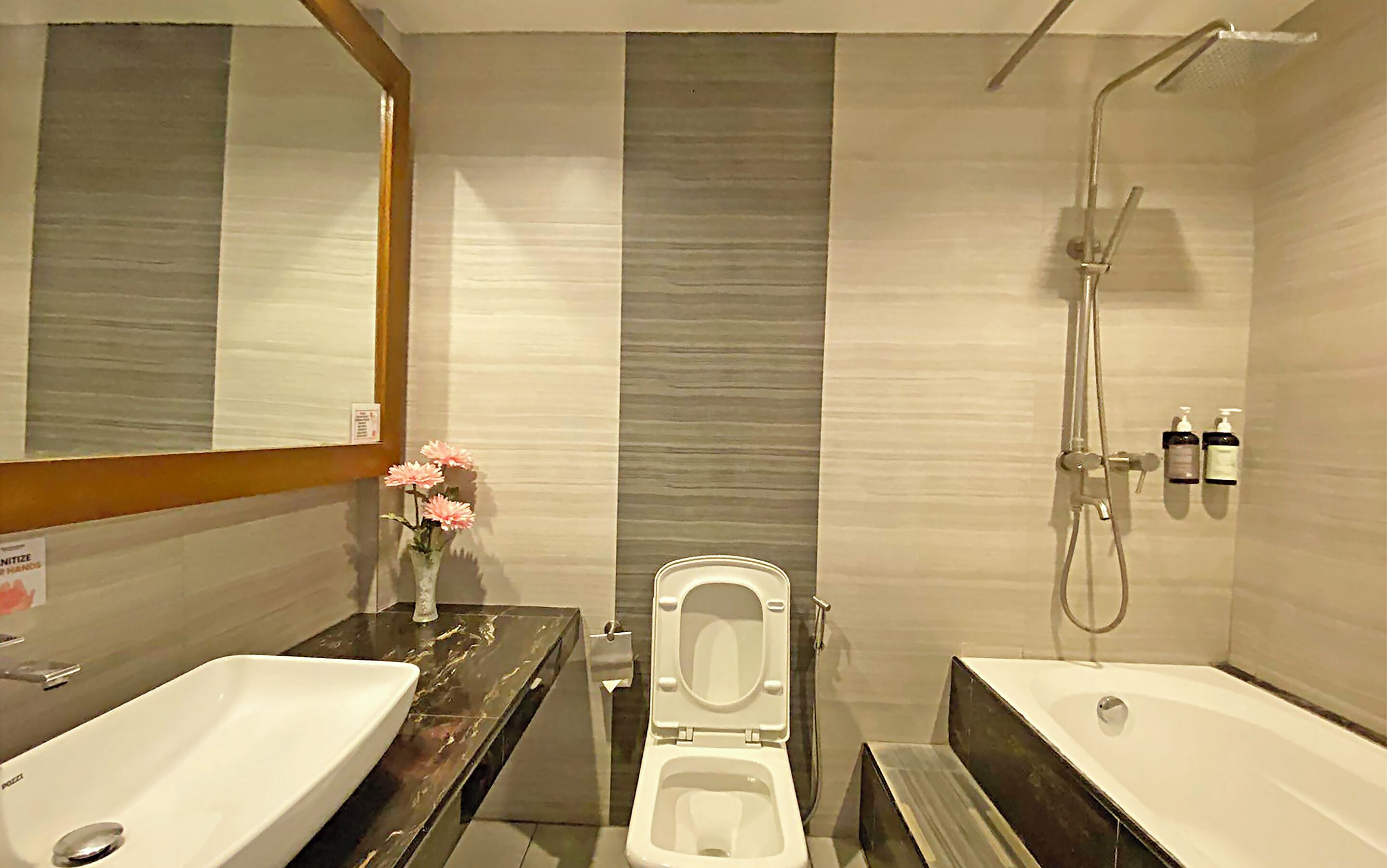 A bathroom with a white toilet, a white sink, and a bathtub. There is a showerhead above the bathtub and a hand dryer on the wall.
