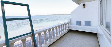 Un balcon avec vue sur la mer, une balustrade blanche et un petit coin salon agrémenté de coussins.