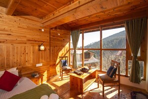 Una acogedora habitación de cabaña de madera con un gran ventanal, una mesa de madera y una cama con almohadones.