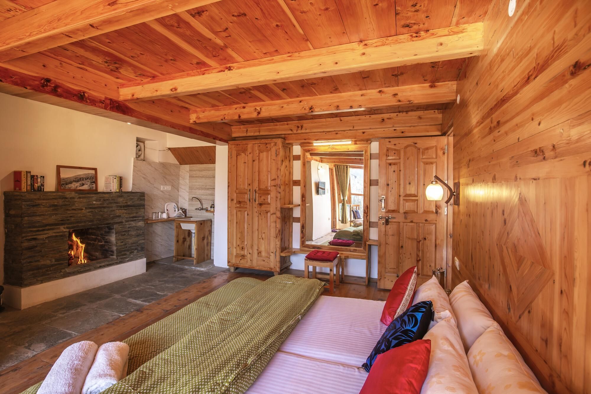A cozy room with a fireplace, wooden walls, a bed with pillows, and a mirror reflecting a window.