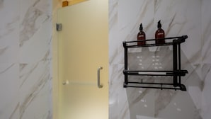A bathroom with a marble wall, a door with a silver handle, and a black towel rack holding two bottles. - Cove Tripuri House Bali (Tuban)