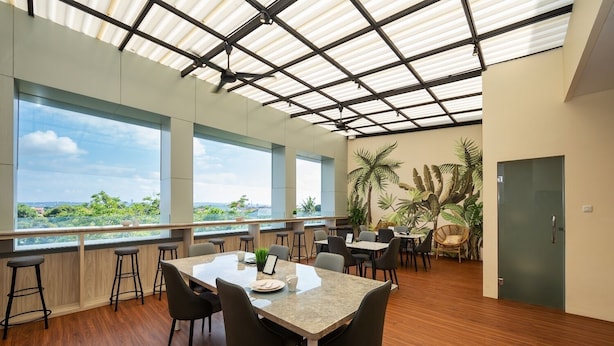 A modern dining area with a large table, multiple chairs, and a view of greenery through large windows. - Cove Tripuri House Bali (Tuban)