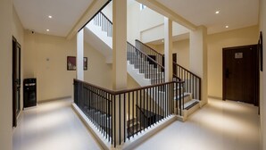 A spacious hallway with a staircase leading to an upper floor, featuring a modern design with a wooden railing and a water dispenser near the entrance. - Cove Tripuri House Bali (Tuban)