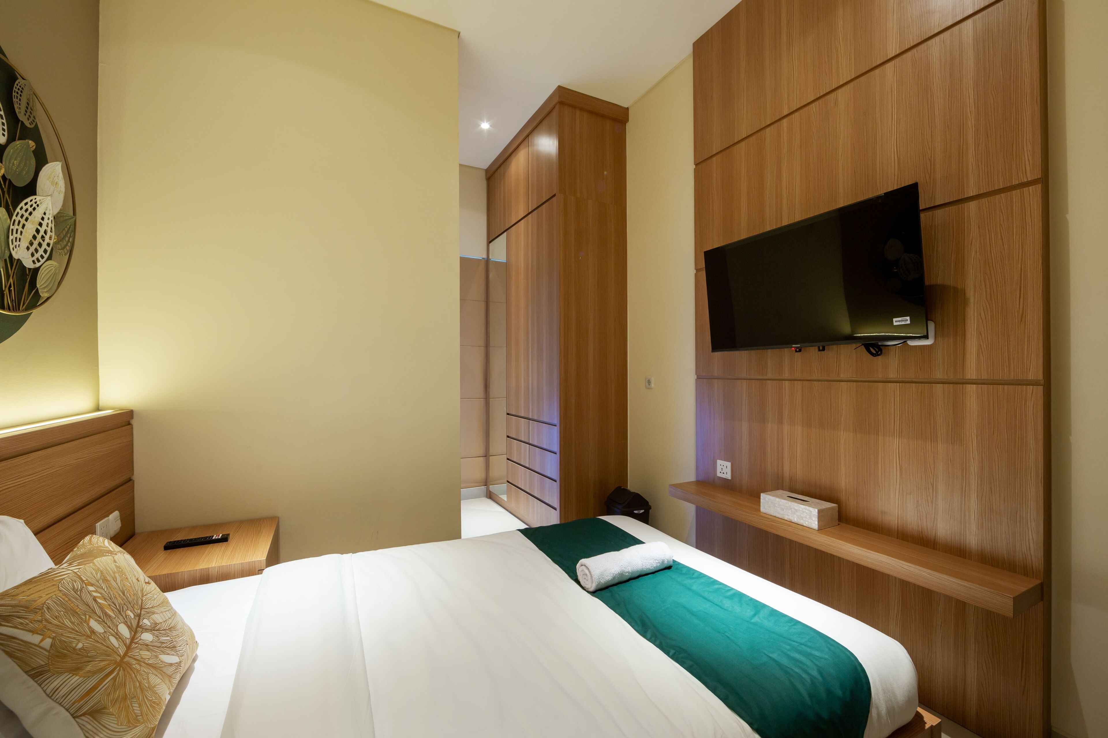 A hotel room with a bed, a TV mounted on the wall, a nightstand, and a wooden wardrobe.