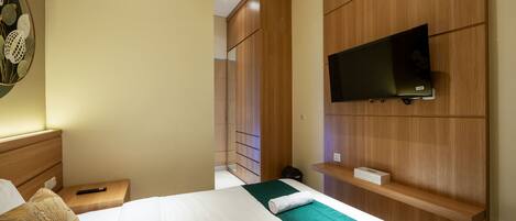 A hotel room with a bed, a TV mounted on the wall, a nightstand, and a wooden wardrobe.