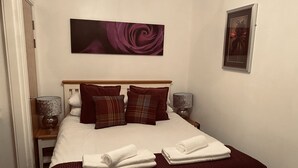 A neatly made bed with a dark red bedspread, two white towels, and three pillows in a hotel room. - 1 Bed Flat - Sleeps 2 - Parking - Wifi (Scarborough)