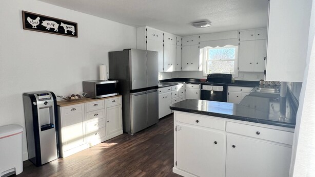 A modern kitchen with white cabinets, stainless steel appliances, and a wooden floor. - An escape to Sister's Haven (Pine City)