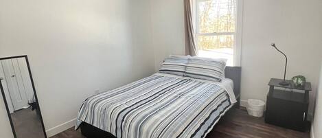 A bedroom with a bed, a window, a nightstand, and a door.