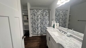 A bathroom with a white vanity, a large mirror, and a shower with floral curtains. - An escape to Sister's Haven (Pine City)