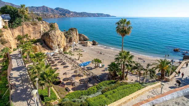 Un resort costero con playa, palmeras e impresionantes acantilados rocosos.