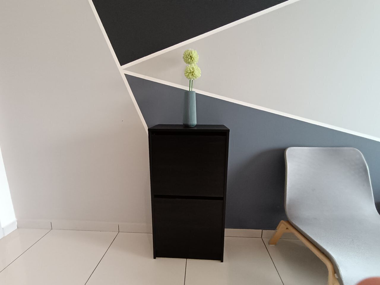 A modern room with a black filing cabinet, a grey chair, and a geometric wall design.