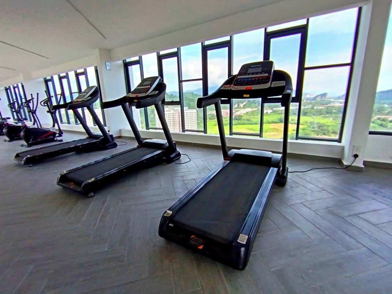 A gym with treadmills aligned against a wall with large windows overlooking a landscape.