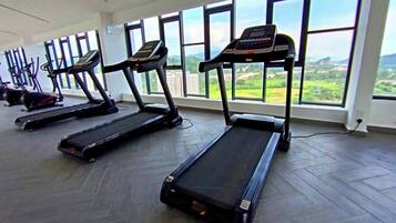 A gym with treadmills aligned against a wall with large windows overlooking a landscape.