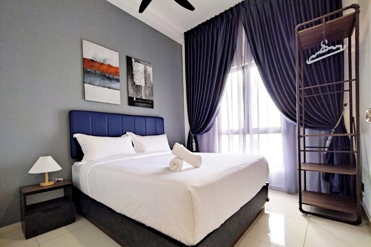 A neatly made bed with white linens, a bedside table with a lamp, and a wall-mounted rack with clothes.