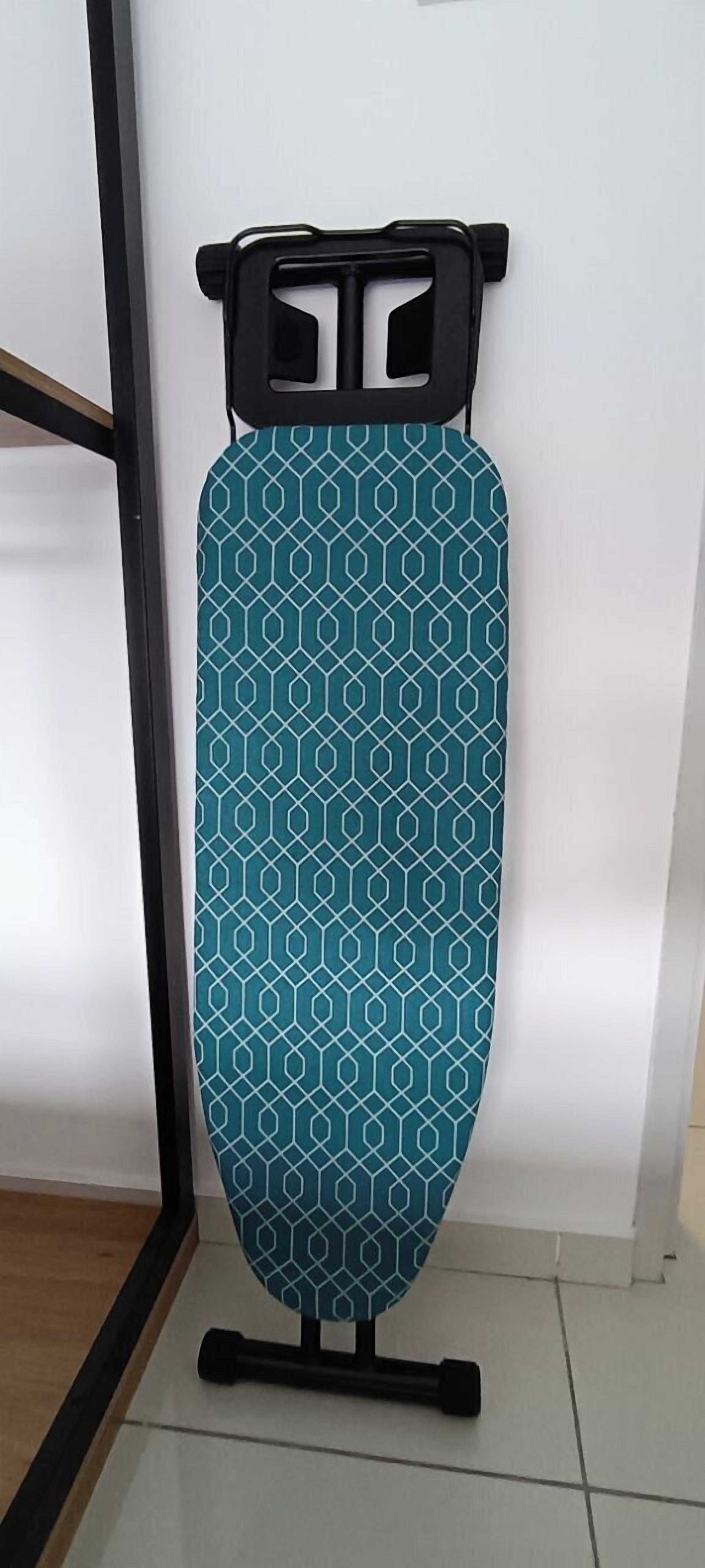 A teal ironing board with a geometric pattern, standing on a black stand, against a white wall.