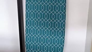 A teal ironing board with a geometric pattern, standing on a black stand, against a white wall.