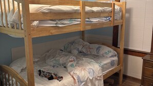 Ein Stockbett mit Holzrahmen, darunter ein Bett mit weißer Bettdecke und ein Fenster mit Jalousien.
