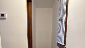 Ein schmaler Flur mit einem gemusterten Teppich, Holzdielen und einem Fenster mit Jalousien.