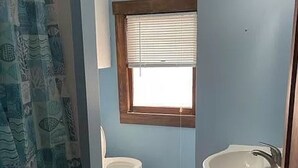 Ein Badezimmer mit Toilette, einem Fenster mit Jalousien, einem Waschbecken und einer Duschvorhang.