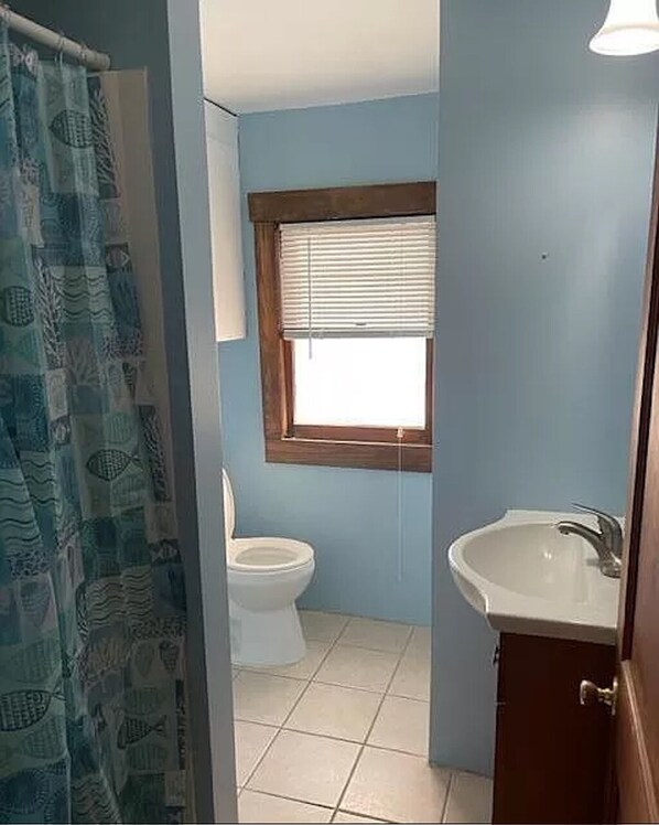 Bathroom features a toilet, sink, and shower with a fish-patterned curtain.