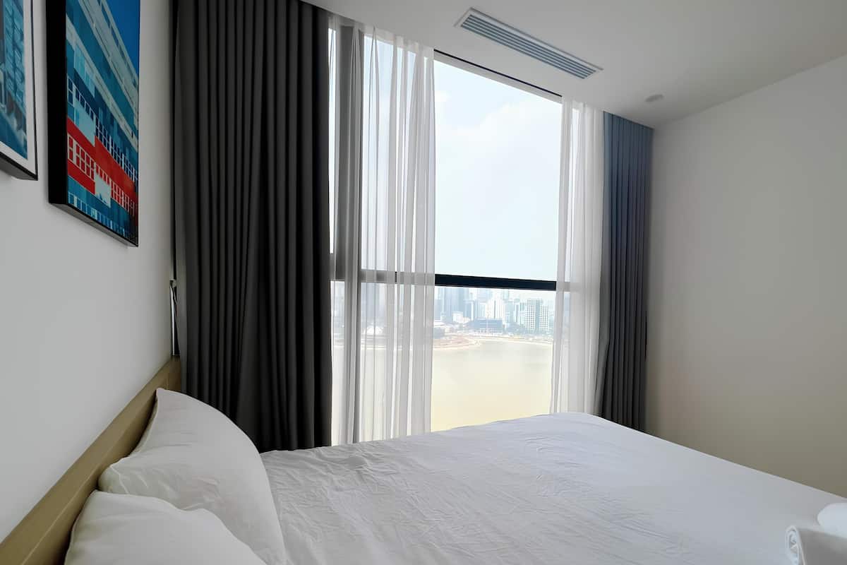 Ein Hotelzimmer mit einem großen Bett, Blick auf die Stadt durch raumhohe Fenster und einem Gemälde an der Wand.