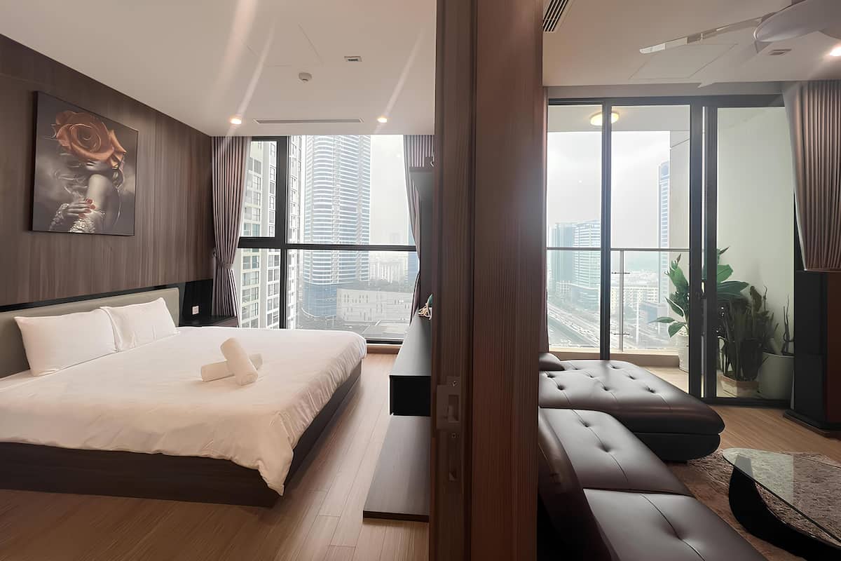 Ein modernes Schlafzimmer mit einem großen Bett, einer Couch und Blick auf hohe Gebäude.