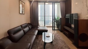 A modern living room with a leather sofa, a glass coffee table, a flat-screen TV, and a ceiling fan. - HKG-Vinhomes Sky Lake - Luxury Apartment (Hanoi)