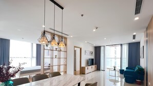 A modern hotel room with a large dining table, comfortable seating, a TV, and a view of the city. - HKG-Vinhomes Sky Lake - Luxury Apartment (Hanoi)