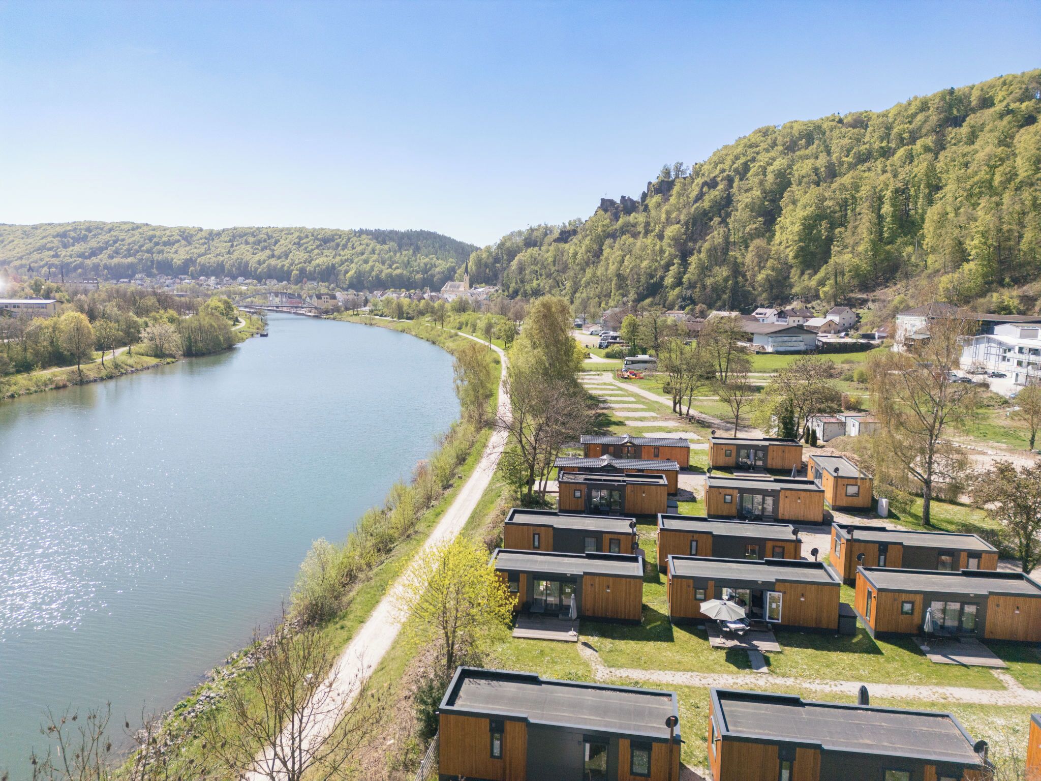 Une vue sur la rivière, avec des cabanes en bois, un ciel dégagé et une colline boisée.