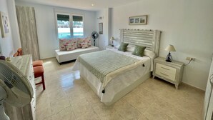 A bedroom with a bed, bedside tables, a fan, a window, and a view of the outside.