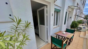 A small outdoor patio with a table and chairs, a potted plant, and a sliding glass door leading to an interior room.