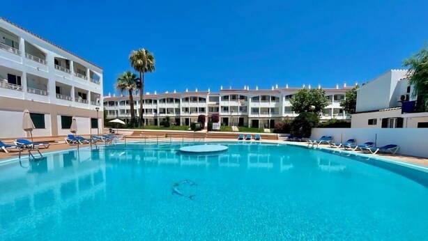 A clear blue pool with lounge chairs and a building with balconies in the background.