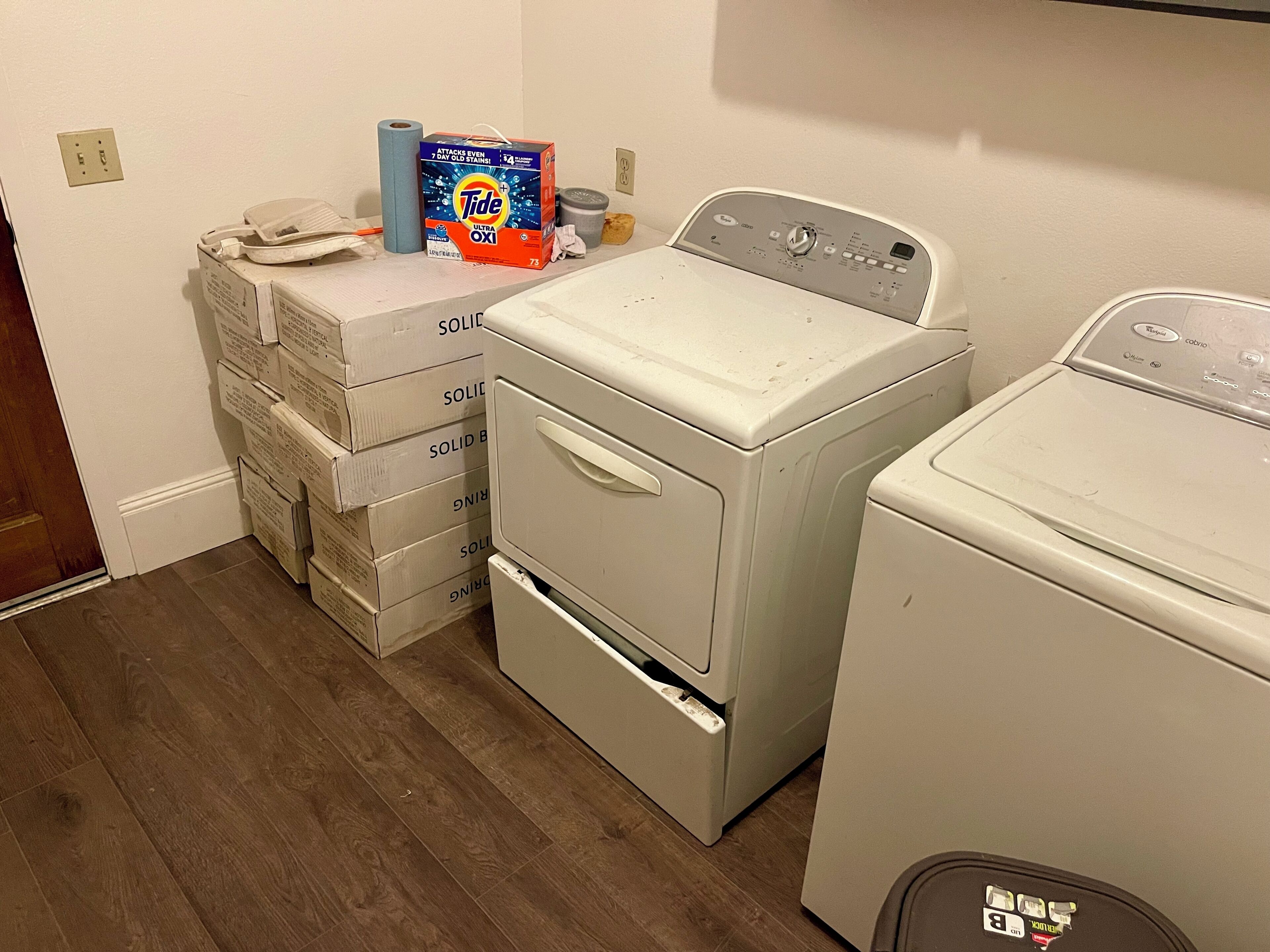 Una sala de lavandería con cajas de detergente apiladas, una lavadora de carga frontal y una secadora.