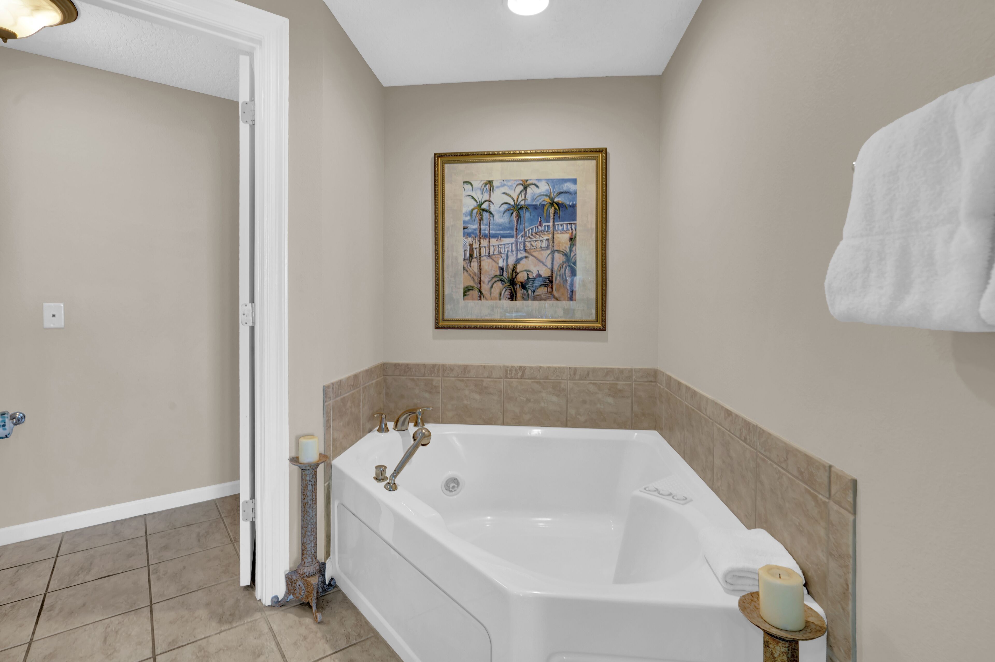 A bathroom with a large bathtub, a framed painting on the wall, and a towel hanging on the wall.