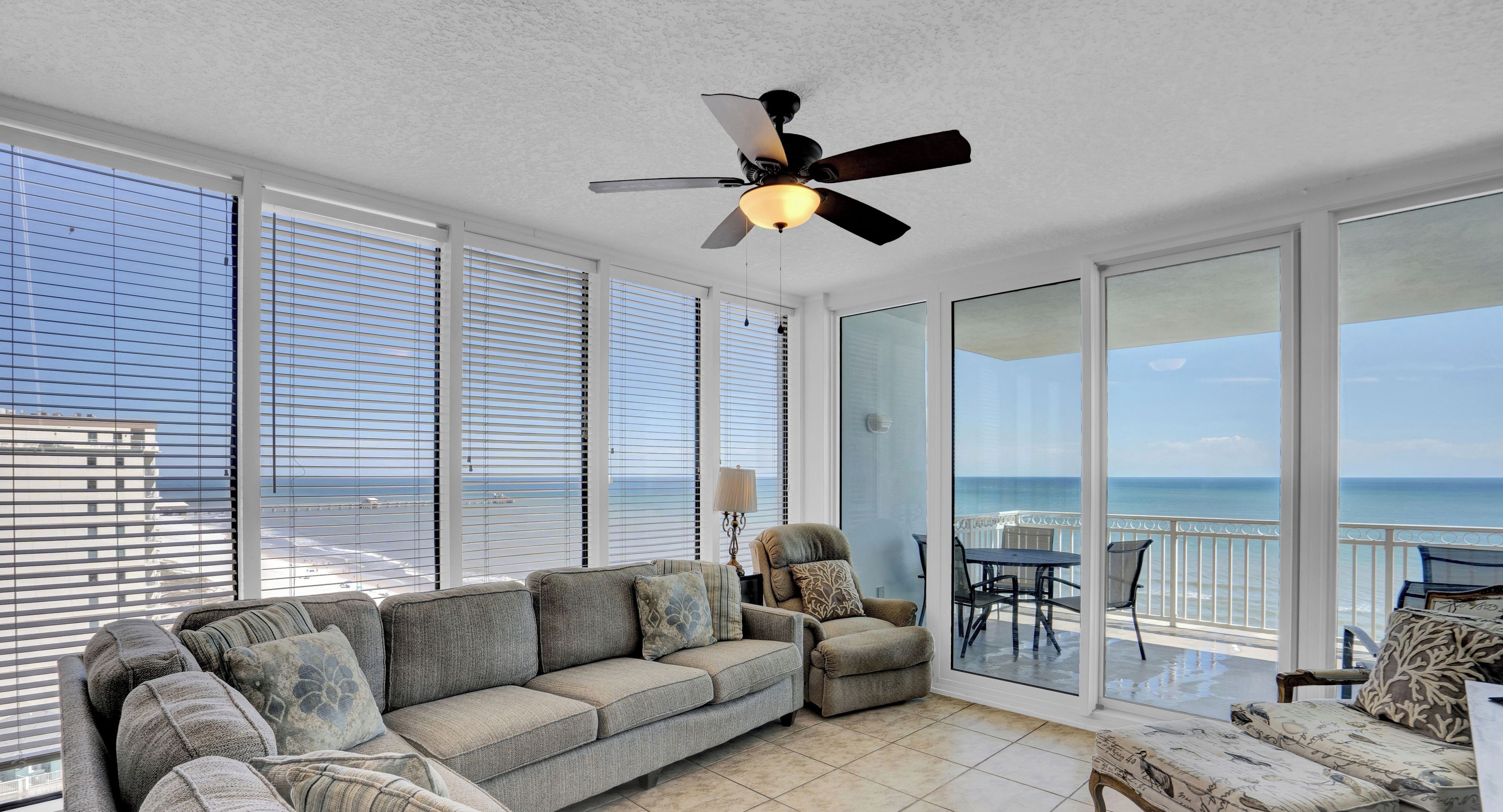 A spacious balcony with a view of the sea, a ceiling fan, and a seating area with a sofa and chairs.