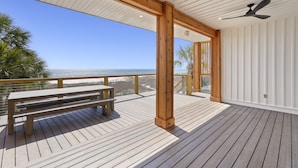 Une terrasse en bois avec un banc, donnant sur une plage et l’océan.