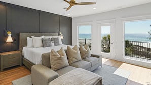 Une chambre à coucher comprenant un lit, des tables de chevet, un canapé, un ventilateur de plafond et un balcon avec vue sur l’océan.