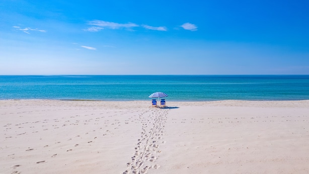 Une plage où l’on voit des empreintes de pas menant à un parasol bleu et blanc.