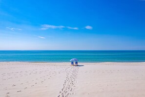A beach with footprints leading to a blue and white umbrella.