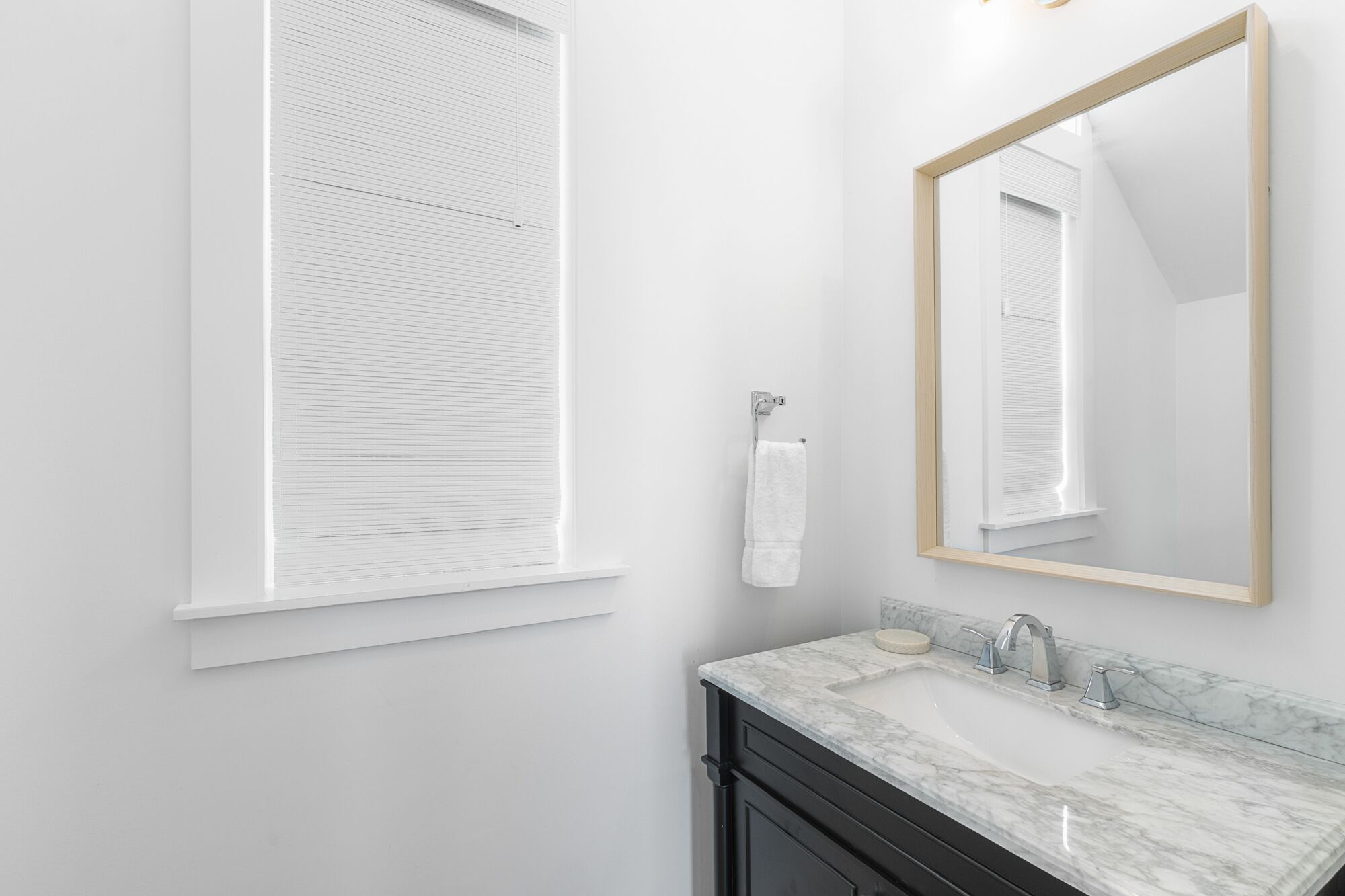 A bathroom with a white vanity, a marble sink, a large mirror, and a window with blinds.